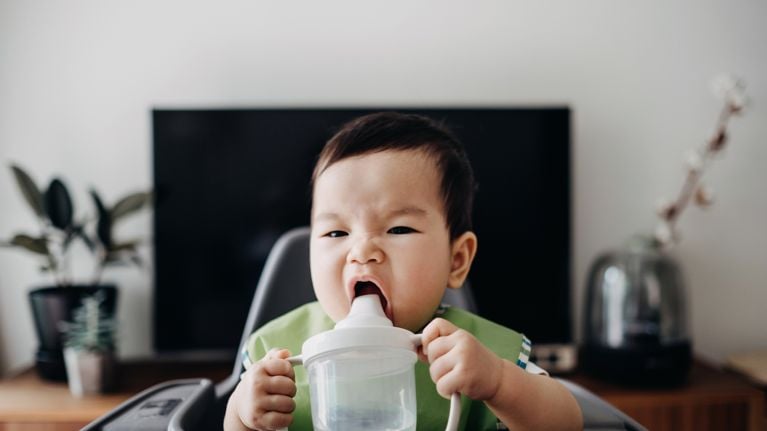 Cute baby drinking water from sip cup on high chair